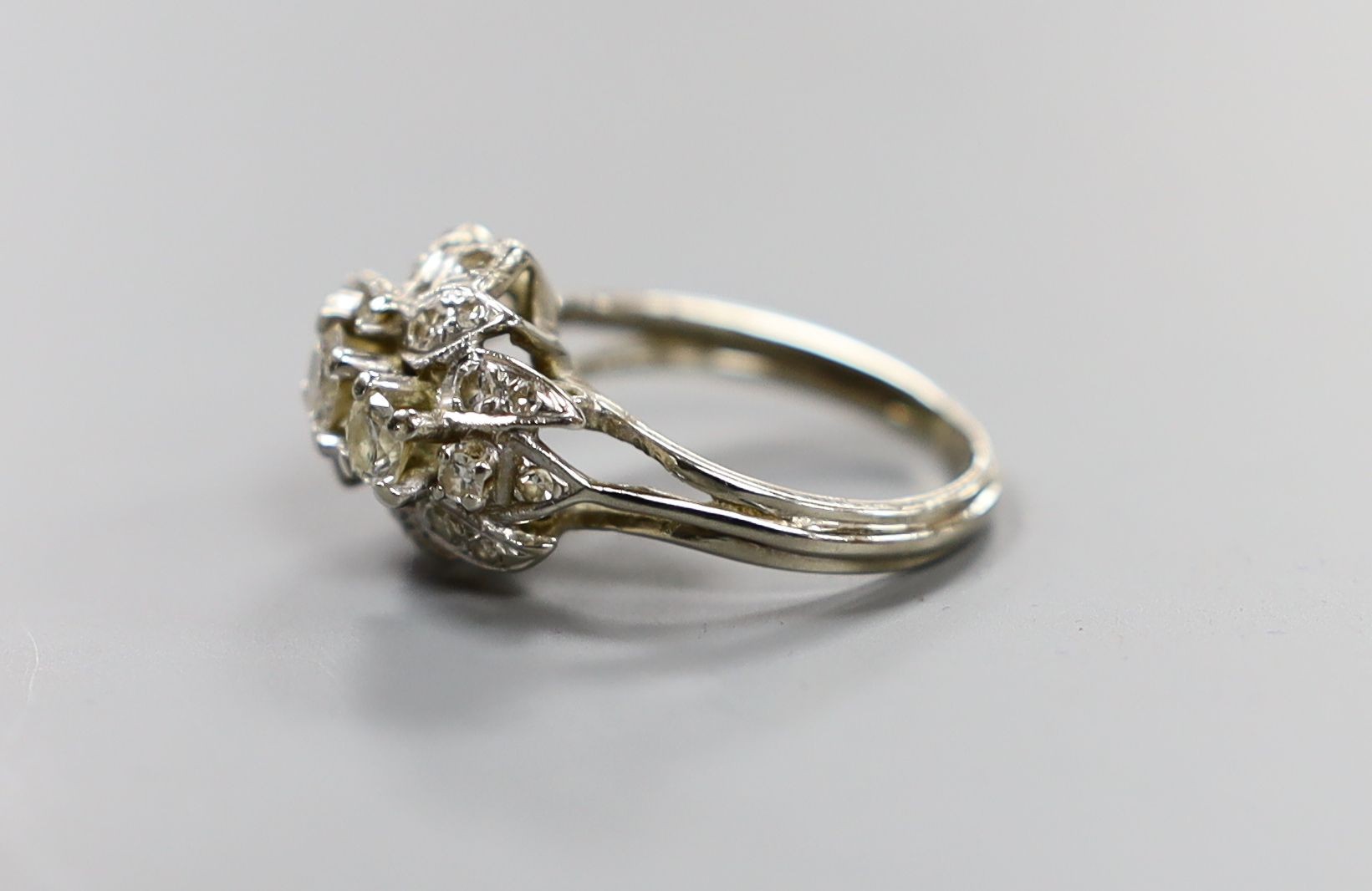 A white metal and three stone diamond ring with diamond cluster setting, size M, gross weight 4.4 grams.